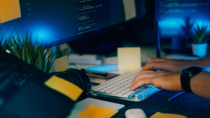 Hands typing on a keyboard with computer screens